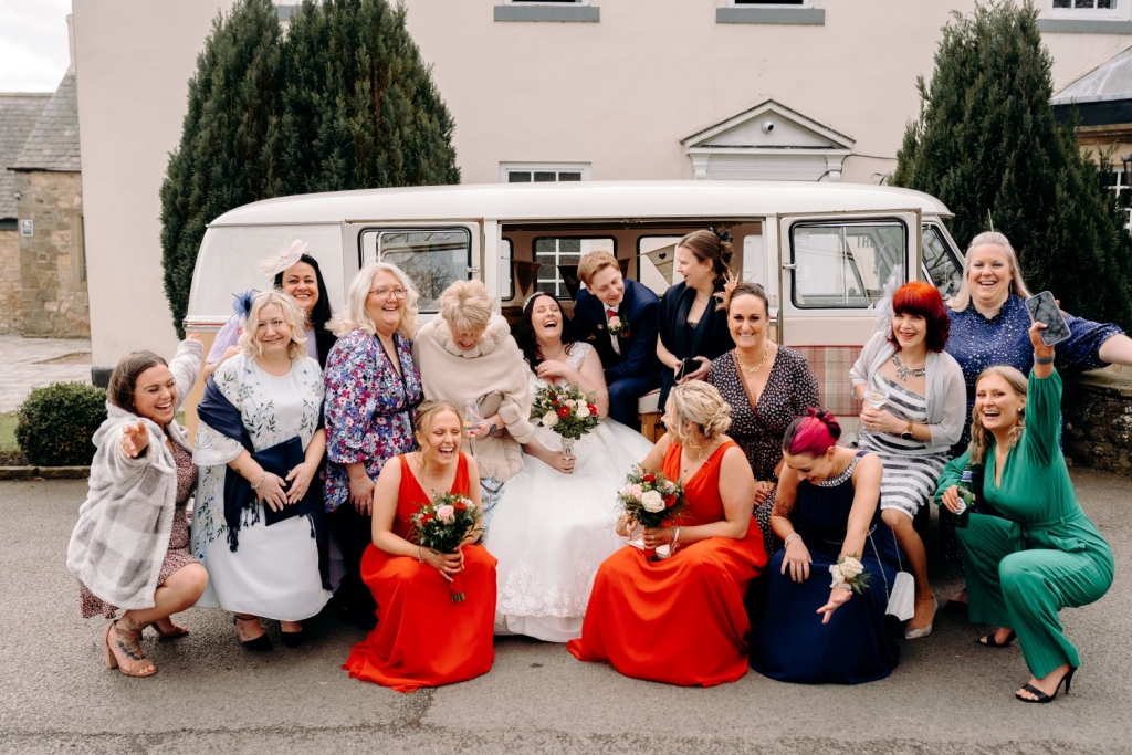 Group shot of full wedding party including bride and groom at Hallgarth Manor in Durham in front of VW Campervan